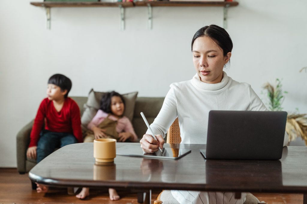 Woman works while her children sit behind her on a couch