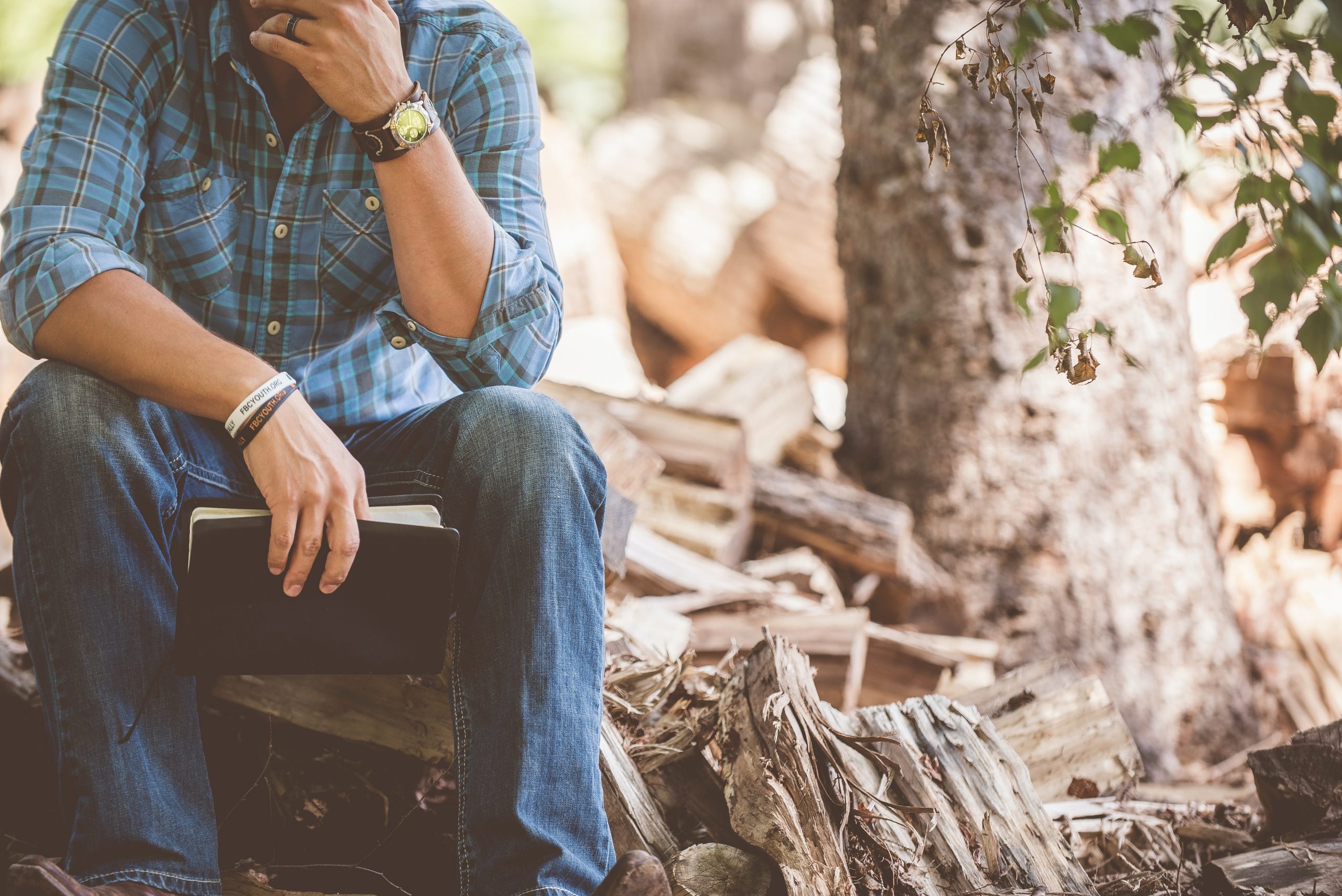 man thinking while sitting on a log and holding a Bible