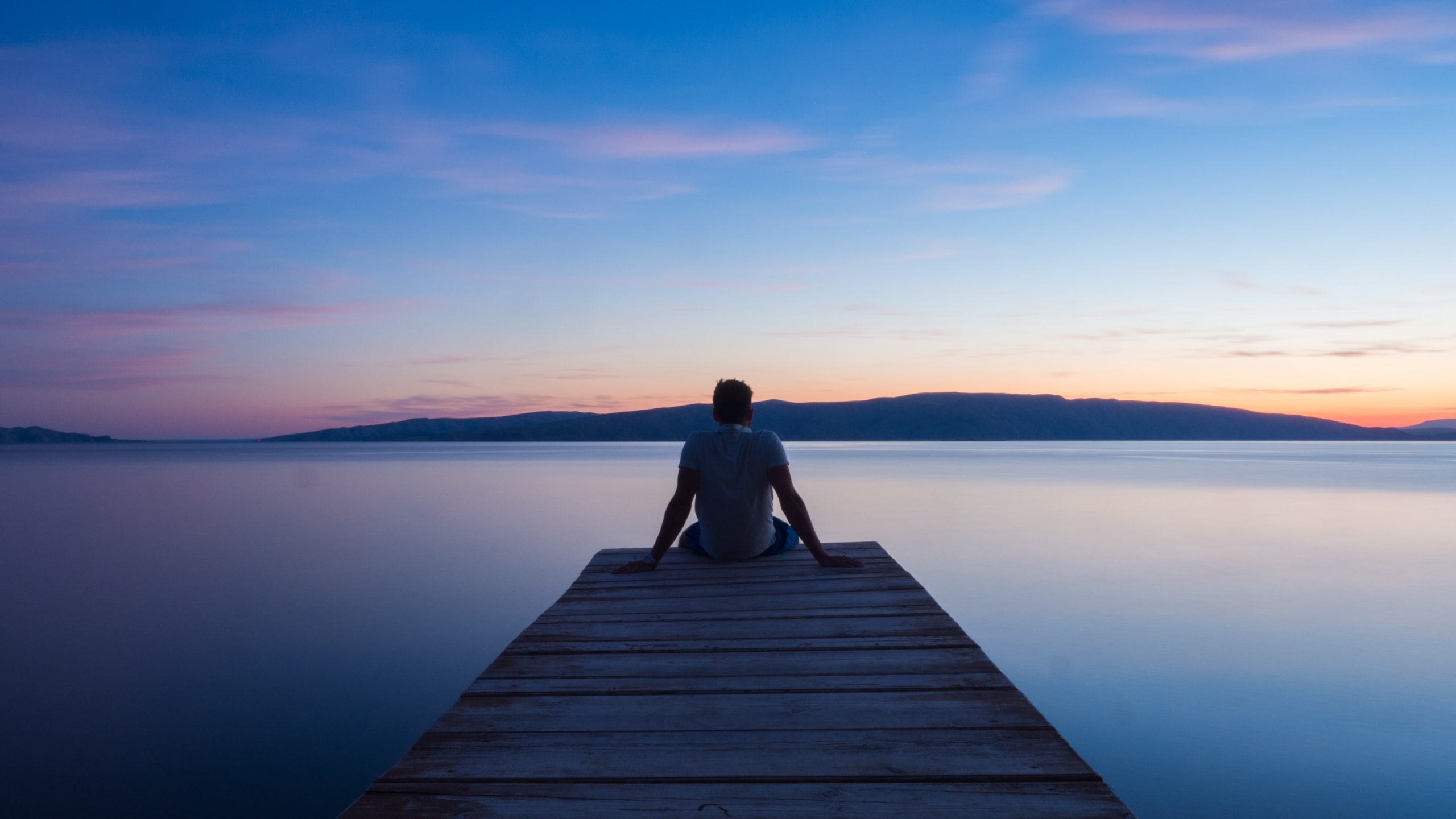 man sitting on deck looking out over water at sunrise