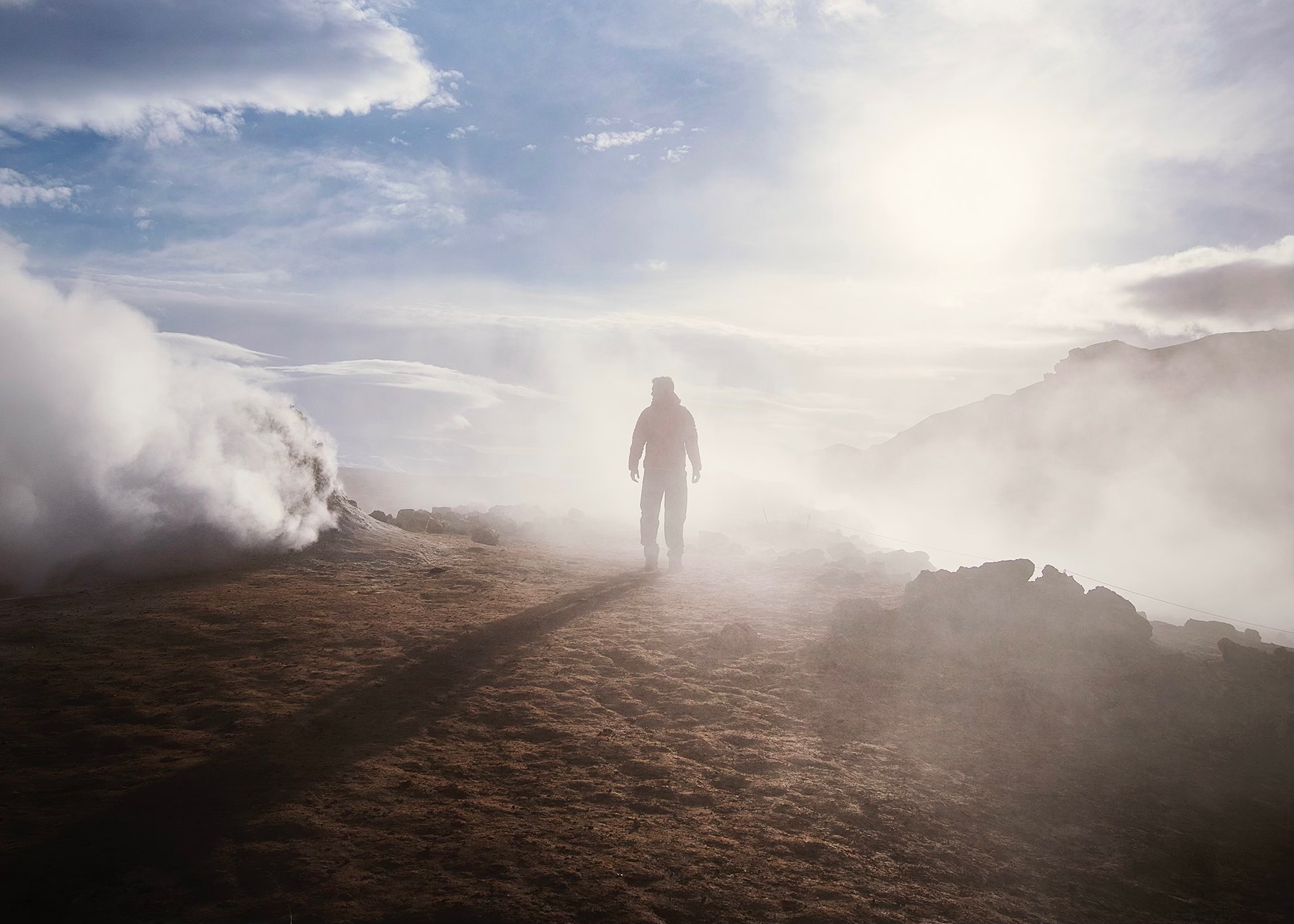 man stand on cliff in fog with glimpses of blue sky and sun