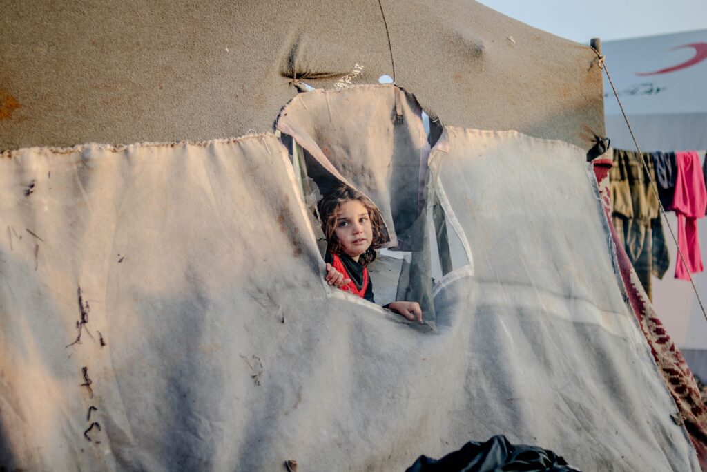 Syrian refugee girl looks out of hole in tent