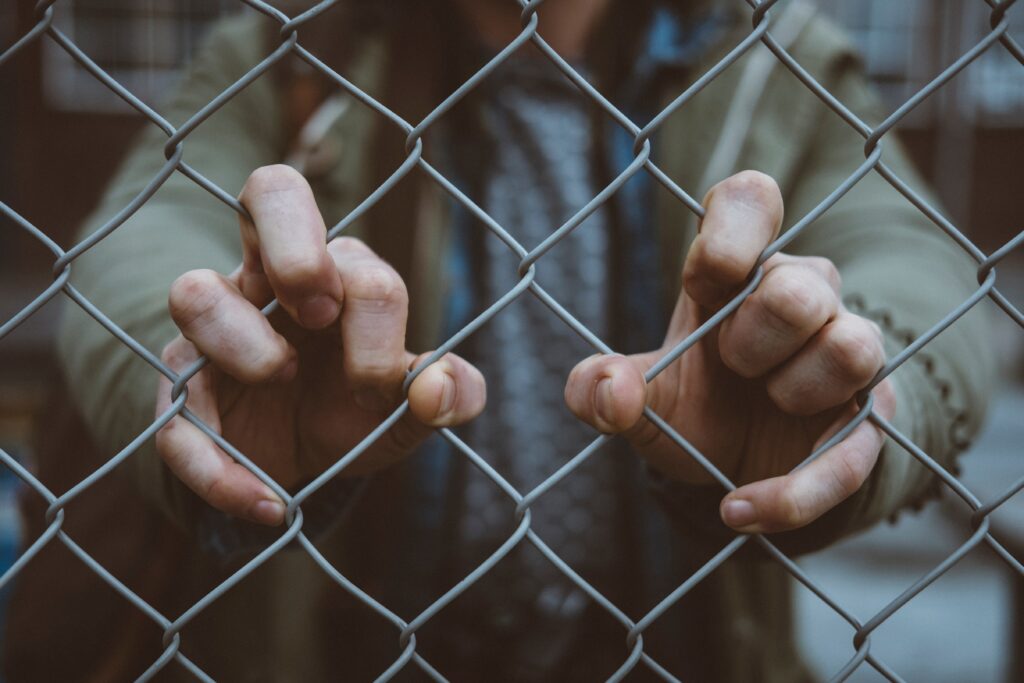 hands gripping chain link fence
