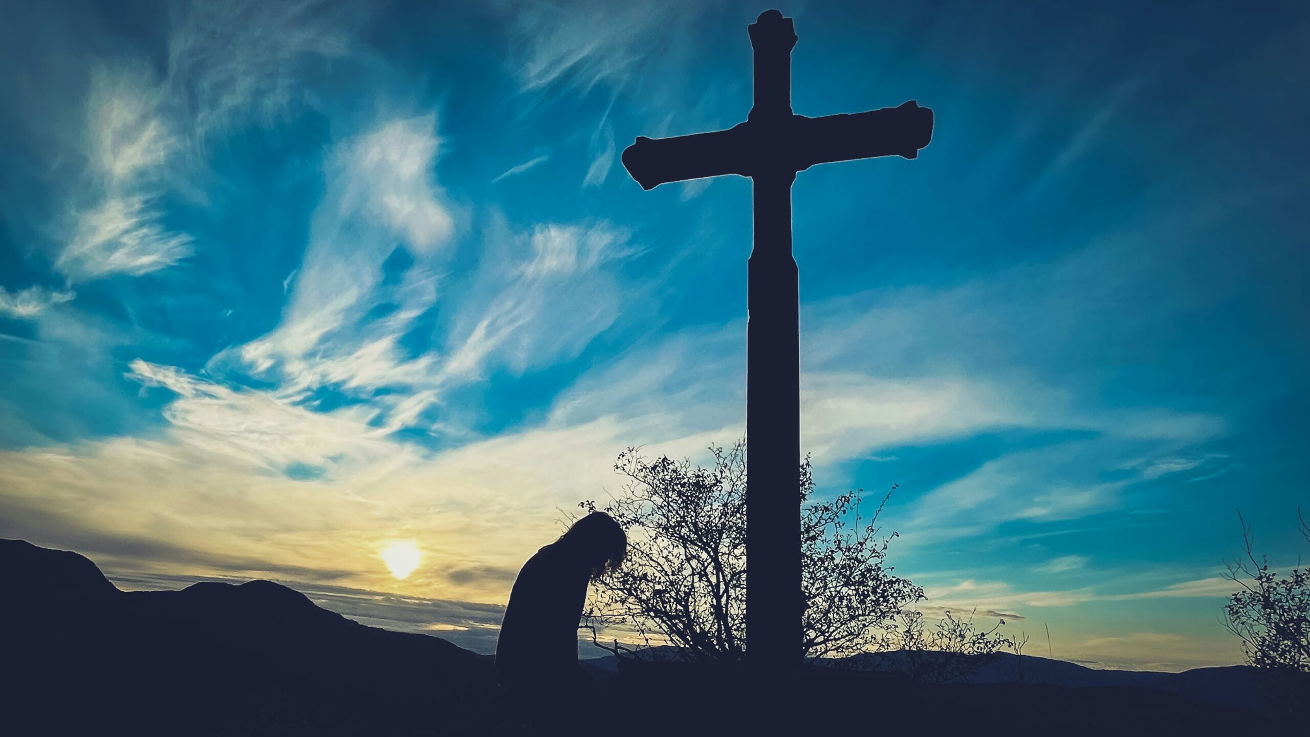 silhouette of someone bowing in front of a cross